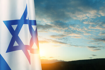 Israel flag with a star of David over cloudy sky background on sunset. Patriotic concept about...