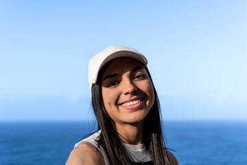 Rostro de mujer latina feliz de cabello negro con gorra y de fondo el mar azul