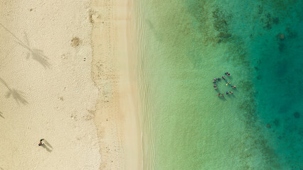 A group of scuba divers training in the ocean. White sand beach in Hawaii top-down aerial drone view. 