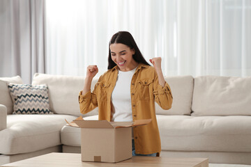 Emotional young woman opening parcel at home. Internet shopping