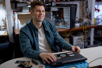 professional young repairman or technician repairs computers and laptop. portrait of service engineer in shirt repairing a laptop, happy guy looking at camera, posing, successful job