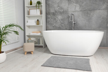 Stylish bathroom interior with ceramic tub, care products and towels in cabinet