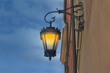 Fototapeta na wymiar Turned on hanging street lamp in old fashion style on building