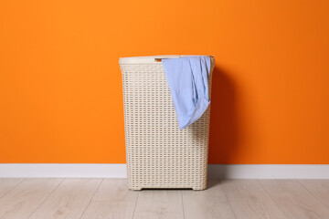Laundry basket with clothes near orange wall indoors