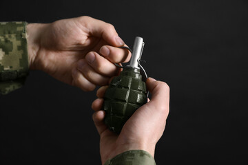 Soldier pulling safety pin out of hand grenade on black background, closeup. Military service - obrazy, fototapety, plakaty