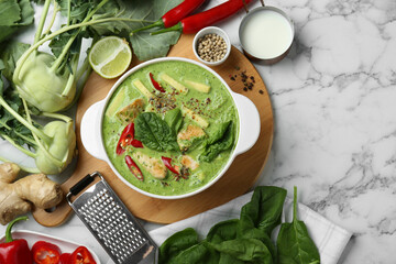 Saucepan with delicious green curry chicken soup and different ingredients on white marble table,...
