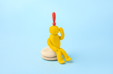 Human figure made of yellow plasticine with exclamation mark as solution idea on light blue background