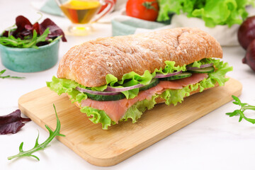 Delicious sandwich with fresh vegetables and salmon on white table, closeup