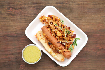 Fresh delicious hot dog with sauce on wooden table, flat lay