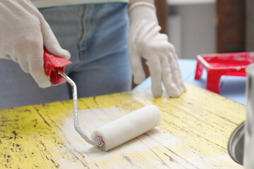 Woman using roller to paint plank with white dye indoors, closeup