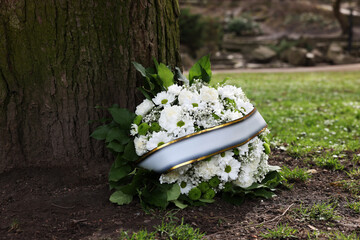 Funeral wreath of flowers with ribbon near tree outdoors