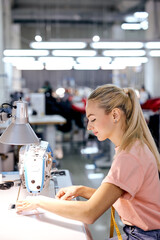 side view on confident beautiful lady working as tailor in textile factory, controlling modern sewing equipment, sit alone at workshop, using textile or clothing. sewing industry concept