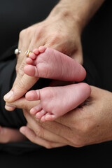 A mother hold the feet of a newborn child in a black blanket on a Black background. The feet of a newborn in the hands of parents. Studio macro photo legs, toes, feet and heels of a newborn.