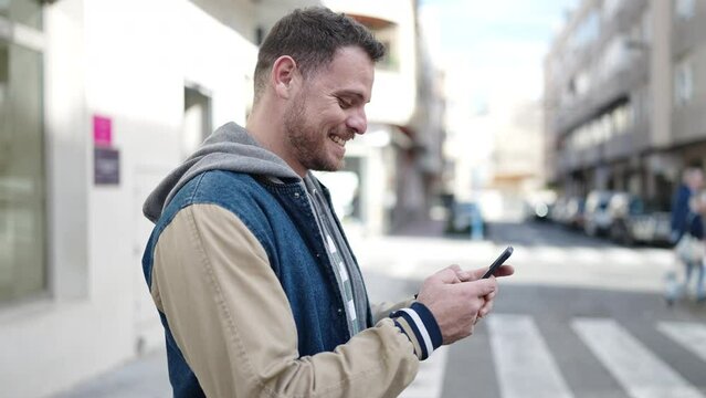 Young caucasian man smiling using smartphone at street