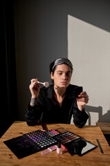 glamour man blowing kiss, holding mirror and brush sitting at the table at home. close up portrait,...