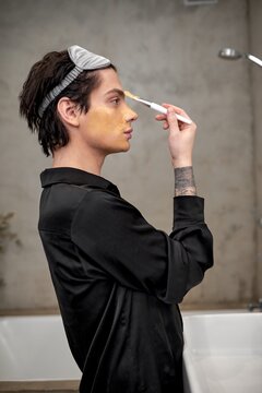young attractive transgender with tattoo on his arm applies cream on his nose, close up side view photo