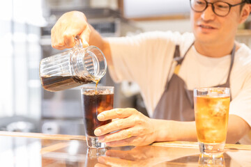 カフェ・飲食店のカウンターでコーヒをグラスに注ぐ店員・キッチンスタッフの男性

