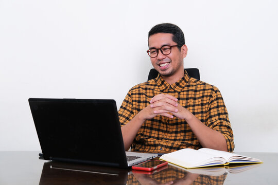 Asian man sitting on working desk smiling relax while looking to his laptop