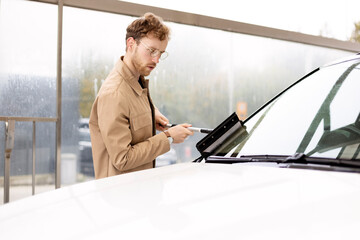 Serious man washing his car with window scraper at self-service station. Employee wiping car