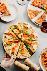 Traditional Italian pizza, vegetables, ingredients on a light background.Top view. a piece of pizza in the hand.Festive table. company of friends
