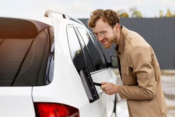 Attractive man thoroughly wiping car with window scraper, he wiping off all drops
