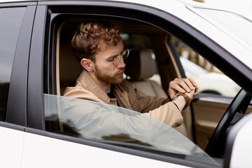 Serious man in casual clothes sitting in car, looking at his watch, checking time. Successful...