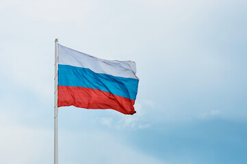 Large Russian flag close-up against a cloudy sky. State symbol of the Russian Federation in the wind.
