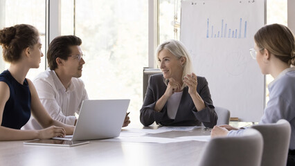 Positive confident middle aged business leader woman meeting with team in boardroom, talking to...