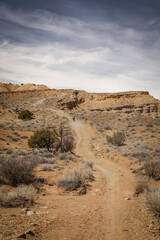 Wide dirt road through desert terrain in spring in central Utah near Goblin Valley underneath  rocky cliffs and mesas