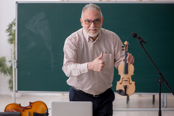 Old male teacher playing violin in the classroom