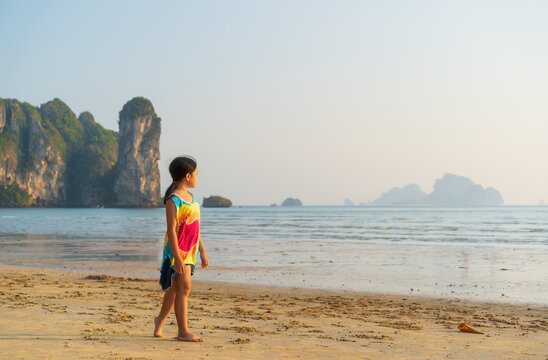 asian child summer or kid girl walking barefoot on sand beach or sea in morning or evening sunlight for tourist people vacation travel and family holiday relax with island at Ao Nang Krabi in Thailand