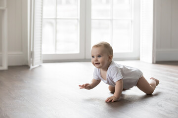 Happy baby in bodysuit crawling on knees on clean warm floor. Cheerful active little infant kid...
