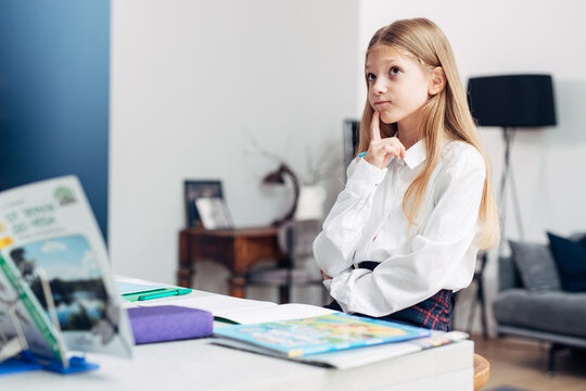 Girl sits thoughtfully at home while doing her lessons, remembering or memorizing information