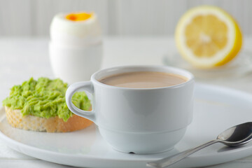 A cup of coffee with cream and a soft-boiled egg with an avocado sandwich on the table. European breakfast.