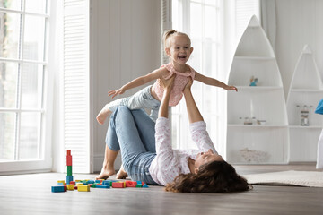 Cheerful excited kid girl and happy mom playing airplane flight, doing acroyoga support, having fun...