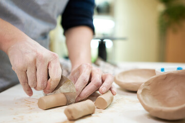 Woman cutting clay with blade standing behind table in studio