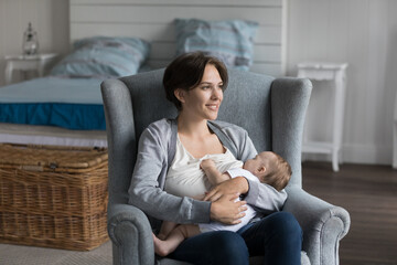 Positive new mom feeding baby milk from breast, looking away, thinking, dreaming, smiling, enjoying...