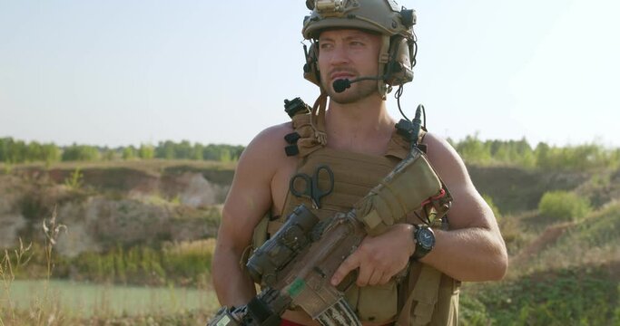 Armed brutal muscular shirtless man in a military uniform holding gun standing on mountains and looks suspiciously around slow motion