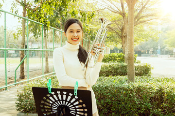 Portrait pretty asian music teacher standing and practicing playing the trumpet with sheet music,...