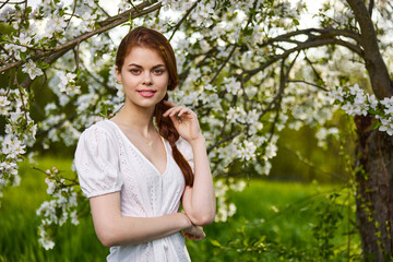 portrait of a young beautiful woman in a white dress among the branches of a flowering apple tree