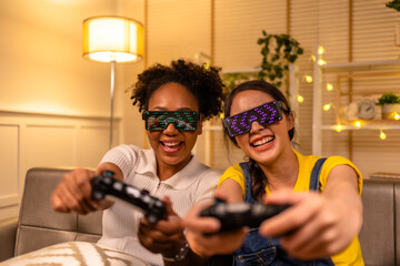 Young  asian and african woman playing video games at home living room at night.Lesbian couples or...