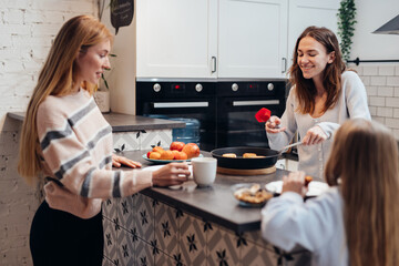 Young mother, friend and daughter gathered to eat freshly made pancakes