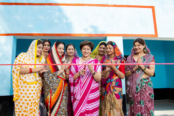 Fototapeta na wymiar Indian woman in sari cutting red ribbon while colleagues are clapping hands. Women empowerment.