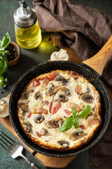 Frittata is an Italian breakfast dish. Omelette with mushrooms and bacon on a dark stone table.