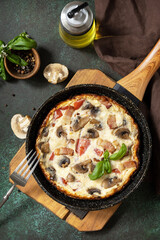 Omelette with mushrooms and bacon on a dark stone table. Frittata is an Italian breakfast dish. View from above.