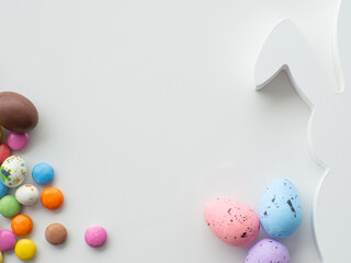 Sweet Easter concept. Colorful and chocolate easter eggs with sweet dragee on white background with copy space. Design for a greeting card for the Easter holiday with bunny. Preparation for holiday.