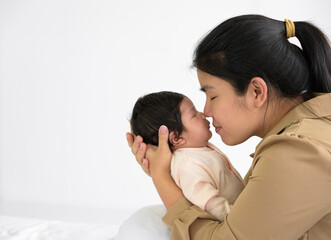 Asian young mom kissing nose of cute newborn little baby. Infant girl or boy sleeping on mom arms on bed at home