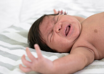 Fototapeta na wymiar Crying newborn baby girl or boy lying on bed.