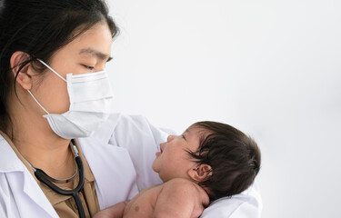 Asian doctor holding cute newborn baby in her arms for physical check up in clinic.