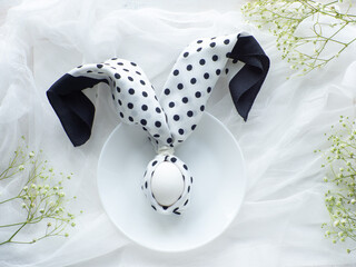 Festive table setting with egg and flowers, flat lay. Easter bunny from black and white napkin. Elegance black and white tablescapes. Easter celebration. Delicate Easter composition. View from above.
